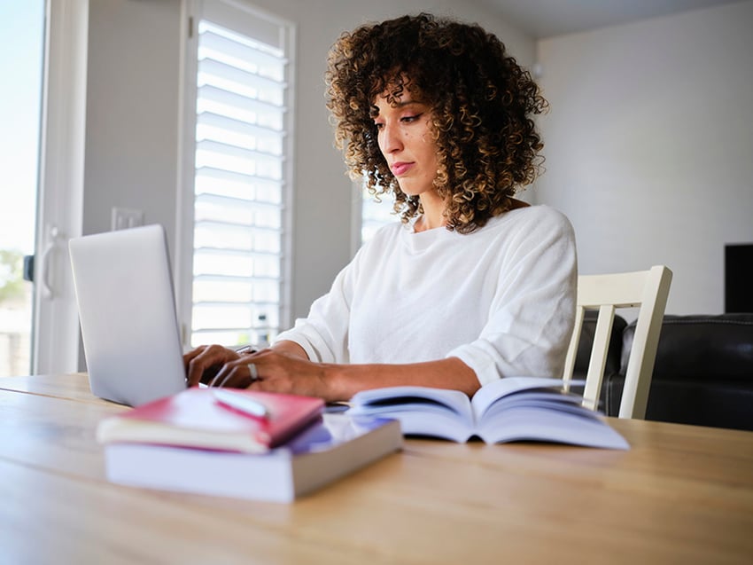 Student with school books open looking at laptop computer